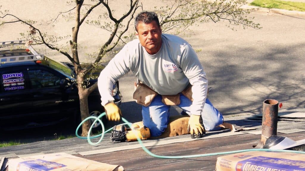 What Makes Nj Roofers of East Brunswick Exceptional Man on a Roof Fastening Roof Shingles with a Nail Gun